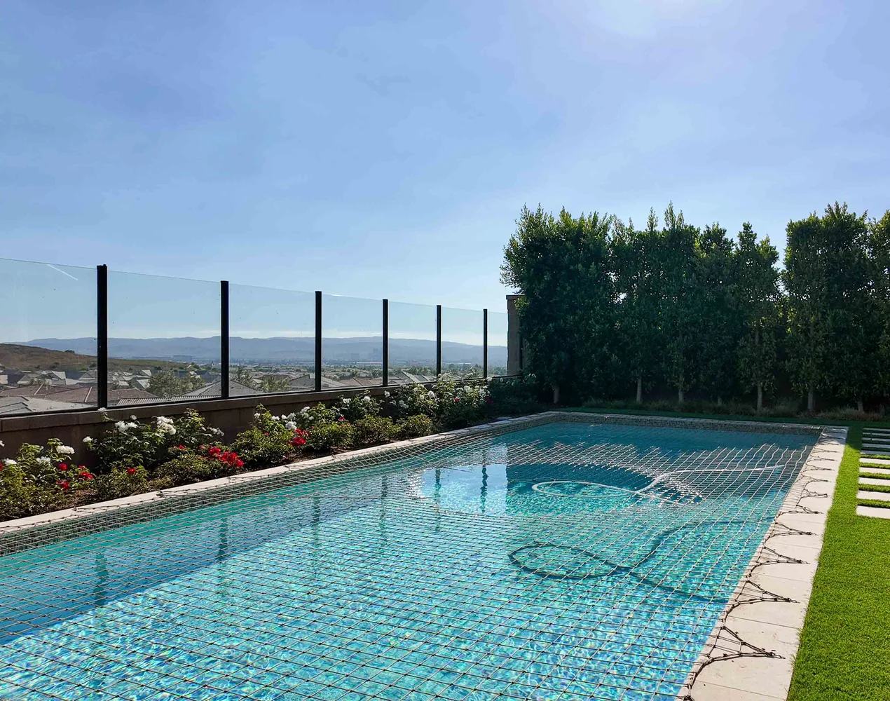 Pool along a frameless glass view railing, with a rose hedge, turf and concrete stepping pads — NHG HOME project, Orange County